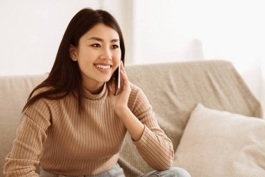 Asyalı Kız Cep Telefonu ve Gülümseyen Talking, Evde Kanepede Oturan, Boş alan