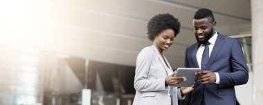 Dijital tablet kullanan ve yeni proje detaylarını açık havada tartışan koyu tenli iş adamları