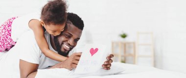 Küçük siyah bir kız, yatağında yatan babasının üzerine eğilir ve ona üzerinde pembe kalp olan bir kart verir. Baba gülümsüyor ve kartı okuyor gibi görünüyor..