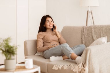 Oturma odasındaki koltukta oturan bir kadın cep telefonuyla konuşuyor..