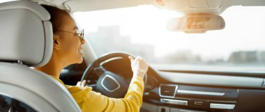 African American woman in sunglasses smiles while driving a car, with her hand on the steering wheel. The view outside the car window is blurred, with a bright sunny sky in the background. clipart