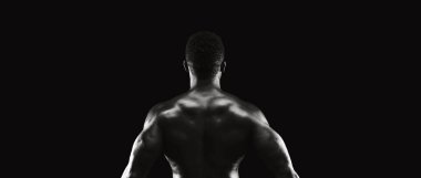 Kaslı bir adam karanlık bir stüdyoda tek bir ışık kaynağı tarafından aydınlatılan kameraya sırtını döner..