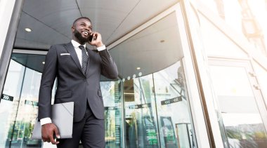 İş Başarı. Şehirdeki ofis girişine karşı cep telefonuyla konuşan Afrikalı Amerikalı adam. Düşük Açı