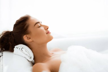 Kadın köpüklü keyifli bir banyo yapıyor, gözleri kapalı yatıyor, boş yer var.