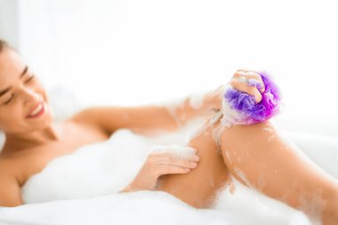 Mutlu kadın bacağını süngerle yıkıyor köpükle banyo yapıyor, küvette dinleniyor.