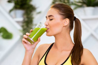 Bir kadın ferahlatıcı yeşil bir smoothie içer. Parlak, modern bir spor salonunda sağlıklı ve ferahlatıcı bir içeceğin tadını çıkarır..
