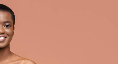 Şeftali rengi arka planda gülümseyen kısa siyah saçlı Afro-Amerikalı genç bir kadının yarım yüzü. Işıklandırma yumuşak ve doğal, özelliklerini vurguluyor, kopyalama alanı