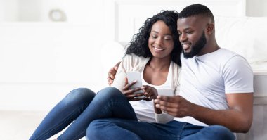 Bir çift kanepede oturuyor, ikisi de akıllı telefonlarını kullanıyor. Kadın telefonuna bakıyor ve gülümsüyor. Adam da telefonuna bakıp gülümsüyor..