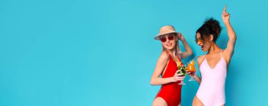 Mayolu iki kadın ellerinde içkilerle kutlama yapıyorlar. Parlak mavi bir arkaplanın önünde duruyorlar, kopyalama alanı olan bir panorama.