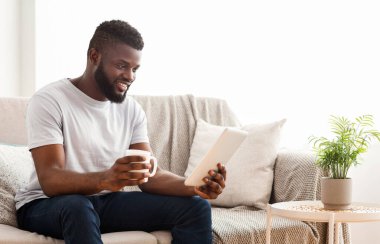 Siyah adam evinde bir kanepede oturuyor, bir fincan kahve ve tabletiyle rahatlıyor. O, yüzünde bir gülümseme ile ekrana bakar. Görüntü, modern boş zamanların iyi bir temsilidir.