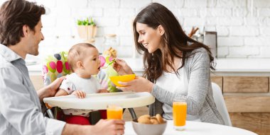 Bir aile mutfaktaki masanın etrafında toplanır ve birlikte yemek yerler. Bir anne bebeğini yeşil bir kaşıkla beslerken, baba da ona bakıp gülümsüyor.