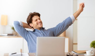 Mavi gömlekli bir adam önünde bir dizüstü bilgisayarla masasına uzanır..