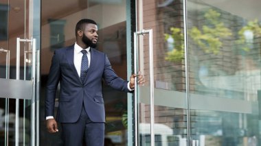 Yakışıklı kendine güvenen Afrikalı işadamı resmi takım elbise modern ofis merkezinden dışarı yürüyüş, kopya alanı