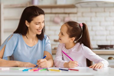 Bir anne ve küçük kızı mutfaktaki bir masada oturuyorlar, renkli kalemlerle boyuyorlar. Birbirlerine bakıp gülümsüyorlar. Bir anlık bağ ve yaratıcılığın tadını çıkarıyorlar..