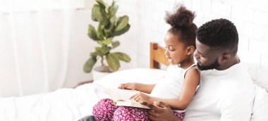 Siyah baba ve küçük kızı bir yatakta oturmuş kitap okuyorlar. Kız babasının kucağında oturuyor ve kitabı işaret ediyor. Babası ona gülümseyerek bakıyor, boşluğu kopyalıyor.