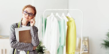 Kendi moda stüdyosunda genç tasarımcı, kameraya poz veriyor ve gülümsüyor.