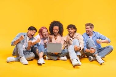 Beş farklı arkadaştan oluşan bir grup sarı bir arkaplanda oturmuş bir dizüstü bilgisayara bakıyor ve kutluyorlar. Hepsi gülümsüyor ve elleri havada..