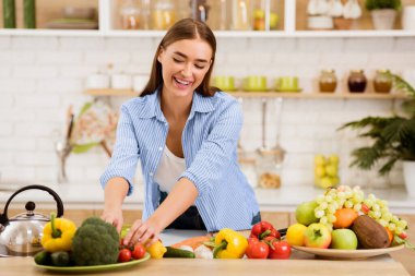 Bir kadın mutfağındaki tabakta taze sebzeleri düzenlerken gülümsüyor..
