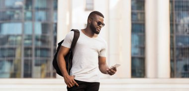 Sırt çantalı genç bir adam şehirde dolaşıp telefonunu kontrol ediyor..