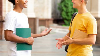 Neşeli öğrenciler dışarıda bir şeyler tartışıyor, üniversite kampüsünde mola veriyorlar.