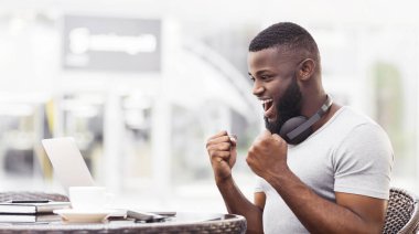 Sakallı bir adam dışarıda bir masada dizüstü bilgisayar kullanarak zaferi kutlar..