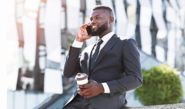 Her zaman temas halinde. Neşeli Afro İşadamı Cep Telefonu Holding Kahve Fincanı Kentsel Alanda Açık Oturan Talking. Boş Alan