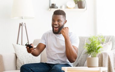 Sakallı genç bir siyah adam oturma odasında bir kanepede oturuyor. Televizyon seyrediyor ve elinde bir kumanda tutuyor. Heyecanlı ve neşeli görünüyor..