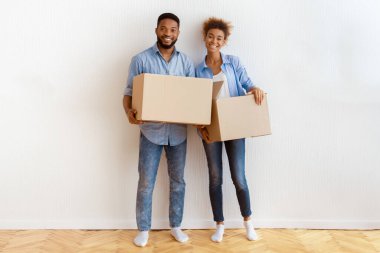 Yeniden yerleştirme. Afrika kökenli Amerikalı eşler taşınma kutularını tutarken Yeni Ev 'de Duvara Karşı Duran Kameraya Gülümsüyor.