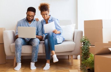 House 'u satın almak. Ciddi Siyahi Çift Dizüstü bilgisayar okuyarak Mülkiyet Kağıtlarını Yeni Evdeki Koltukta Otururken Kullanıyor. Boş Boşluk