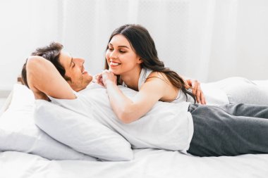 Bir erkek ve bir kadın beyaz bir yatak odasında birlikte yatıyorlar. Kadın yan yatmış, sırtüstü yatan adama bakıyor. Hem gülümsüyor hem de birlikte olmaktan zevk alıyor gibi görünüyorlar..