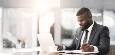 Ciddi Afro İşadamı Laptop Açık Kafede Kahve Molası Sırasında Notlar Alarak Çalışma. Meşgul Gün Konsepti