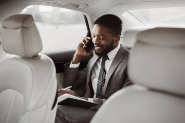 Takım elbiseli Afro-Amerikalı işadamı bir arabanın arka koltuğunda oturuyor. Telefonla konuşuyor ve not defterine not alıyor. Seyahat ederken bir iş görüşmesi yapıyormuş gibi görünüyor..