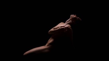 Bir kadın, siyah bir arkaplana karşı dramatik bir şekilde poz verir, vücudu şehvetli bir şekilde kıvrılır. Işıklandırma onun kıvrımlarını vurguluyor, gizem ve cazibe hissi yaratıyor.