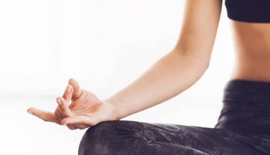Klasik nilüfer pozisyonunda oturan koyu yoga pantolonlu kadın parmakları bir mudra oluşturuyor, sakin bir meditasyon seansına girerken odaklandığını ve sakinleştiğini gösteriyor.
