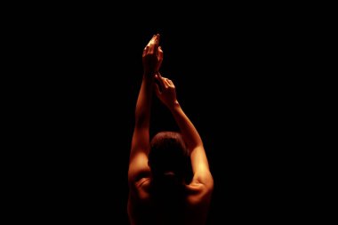 Sahnede, arka planda bir bayan dansçı sahne alıyor. Kolları başının üstünde ve vücudu sıcak, turuncu bir ışıkla aydınlanıyor. Yüzü görünmüyor..