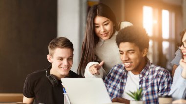 Çeşitli bir grup öğrenci bir dizüstü bilgisayarın etrafında toplanmış, dikkatlice ekrana bakıyorlar. Bir tartışmada ya da içeriği birlikte görüyor gibi görünüyorlar..