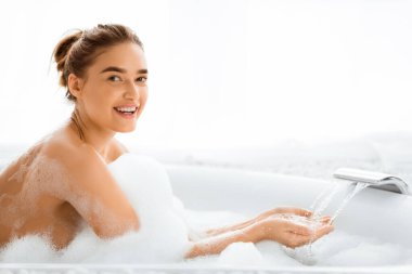 Sıcak banyodan hoşlanan ve akan suyun sıcaklığını ölçen kadın kameraya gülümsüyor.