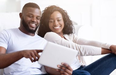 Bir çift kanepede oturuyor, gülümsüyor ve tablet bilgisayara bakıyor. Kadın tableti tutarken adam tableti işaret ediyor..