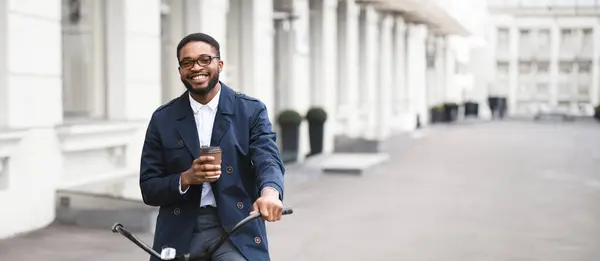 Stock image An African American businessman is on his bike with takeaway coffee. The setting is contemporary and bustling, emphasizing a dynamic and health-conscious approach to commuting.