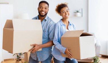 Mutlu Yer Değiştirmeler. Taşınan kutuları taşıyan genç siyah çift Yeni Ev 'de ayakta kameraya gülümsüyor..