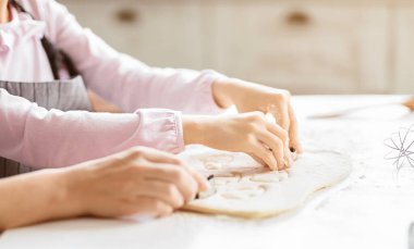 İki insan bir mutfakta, elleri hamurdan şekiller kesmek için birlikte çalışırken görülüyor. Onlar muhtemelen özel bir durum için kurabiye veya diğer hamur işleri yapıyorlar..