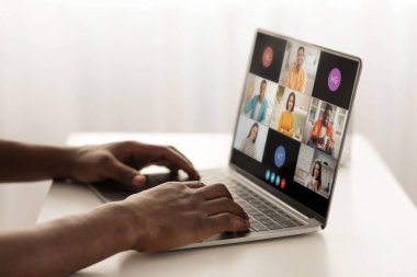 Bir kişi masada oturuyor, birkaç kişiyle video konferansına katılmak için dizüstü bilgisayar kullanıyor. Dizüstü bilgisayar ekranı, her biri farklı bir katılımcıyı gösteren bir video penceresi ızgarası görüntüler
