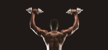 Kaslı bir adam kafasının üstüne iki dambıl kaldırır ve sırt kaslarını gösterir..