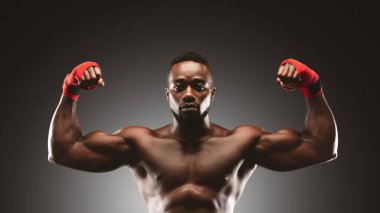 Kırmızı eli olan gömleksiz bir adam stüdyo ortamında pazılarını esnetir..