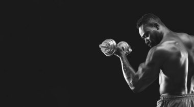 Bir adam sağ koluyla dambılı kaldırır, kasları gerilir..