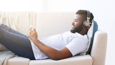 Siyah adam beyaz bir kanepede uzanıyor, kot pantolon ve beyaz bir tişört giyiyor. O, kulaklık takıyor ve müzik dinliyor. Gözleri kapalı ve rahatlamış ve eğleniyor gibi görünüyor..