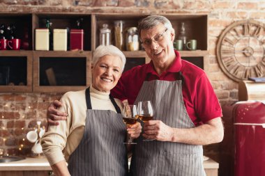Önlük giymiş son sınıf bir çift modern bir mutfakta durup şarap kadehleriyle kadeh kaldırıyor. Gülümsüyorlar ve birbirlerine bakıyorlar, açıkça eğleniyorlar..