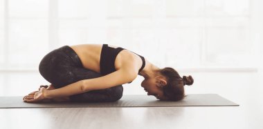 Bir kadın öne doğru eğilip yoga pozu veriyor, gövdesi bacaklarının üzerine katlanmış, elleri öne doğru uzanıyor, ayaklarına dokunuyor, yandan bakıyor.
