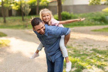 Bir baba, güneşli bir günde kızına parkta sırtına bindirir. Baba gülümsüyor ve kız ileriye bakıyor. İkisi de öğleden sonranın tadını çıkarıyor..