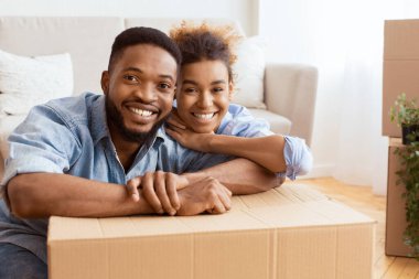 Taşınan kutular arasında kucaklaşan Afrikalı Amerikalı eşler Yeni Ev 'de oturan kameraya gülümsüyor. Boş Boşluk